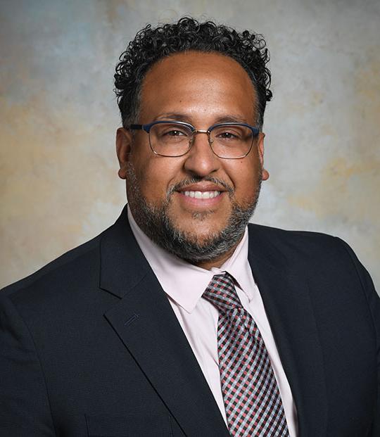 headshot of man with glasses, in suit and tie